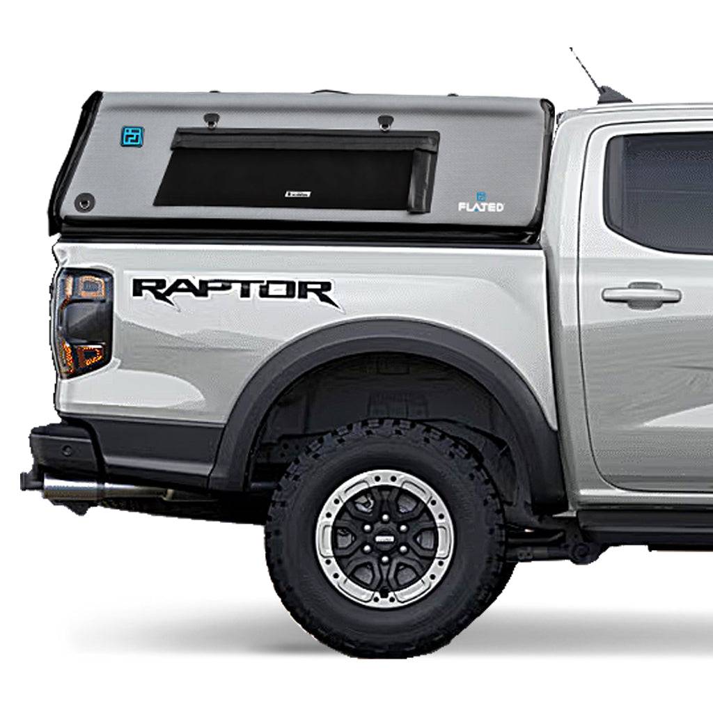 A silver pickup with a black and gray FLATED MID-SHORT CAP411 truck topper on the flatbed. The word RAPTOR appears above the rear wheel, and only the rear half of the vehicle is visible.