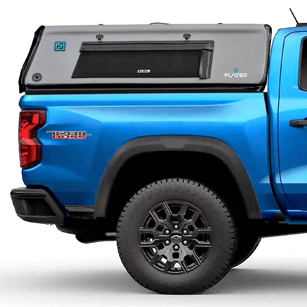 A blue Toyota Tacoma pickup truck with a gray FLATED MID-SHORT CAP50 inflatable truck shell attached to the open cargo area, shown from the side.
