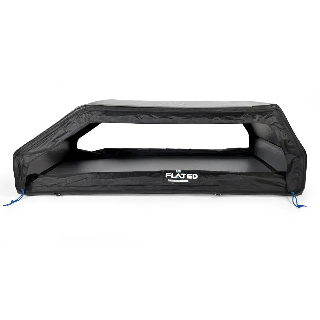The FLATED SPORT CARRIER15 (OPEN BOX) is a black inflatable truck bed cover with angled sides and blue tie-down cords at each corner, ideal for storing outdoor gear. The FLATED brand name appears on the front.