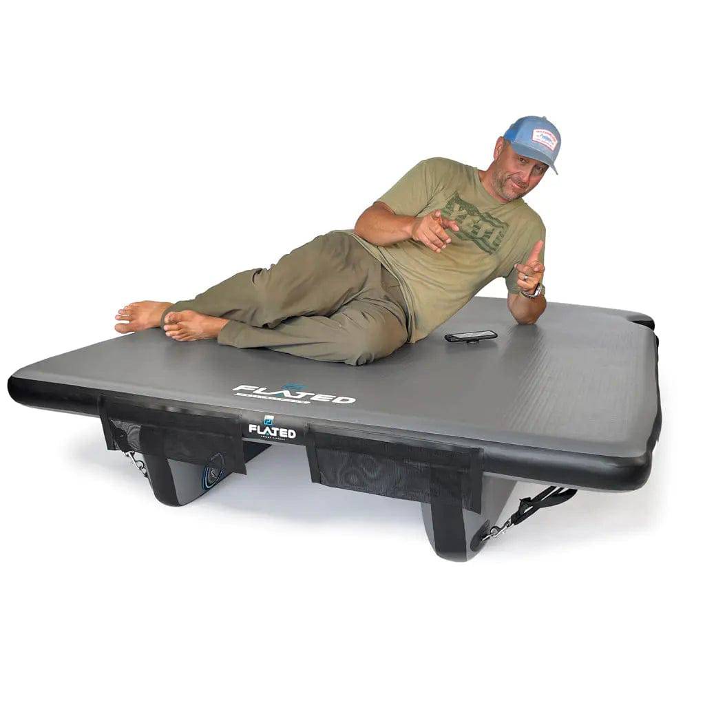 A man in a cap and casual wear lies on the FLATED MID-SHORT DECK50 (OPEN BOX), smiling and gesturing with both hands, highlighting this inflatable truck bed—ideal for any mobile adventure setup.