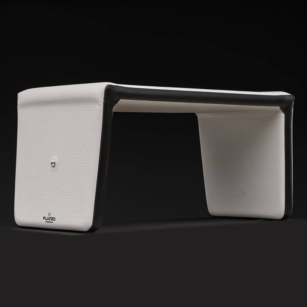 The FLATED MID-SIZE TABLE60 is a modern, minimalist white portable table with black trim and smooth rectangular surfaces, featuring the FLATED logo on one side, shown against a solid black background.