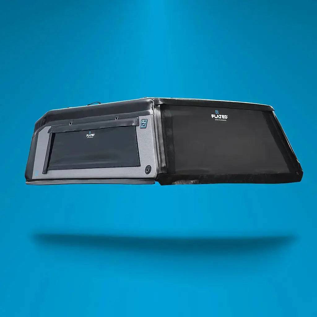 The FLATED MID-SHORT HR MR53 truck bed canopy, black and gray with side-access window and Plastex logo, is shown floating against a solid blue background. Ideal as a truck topper.