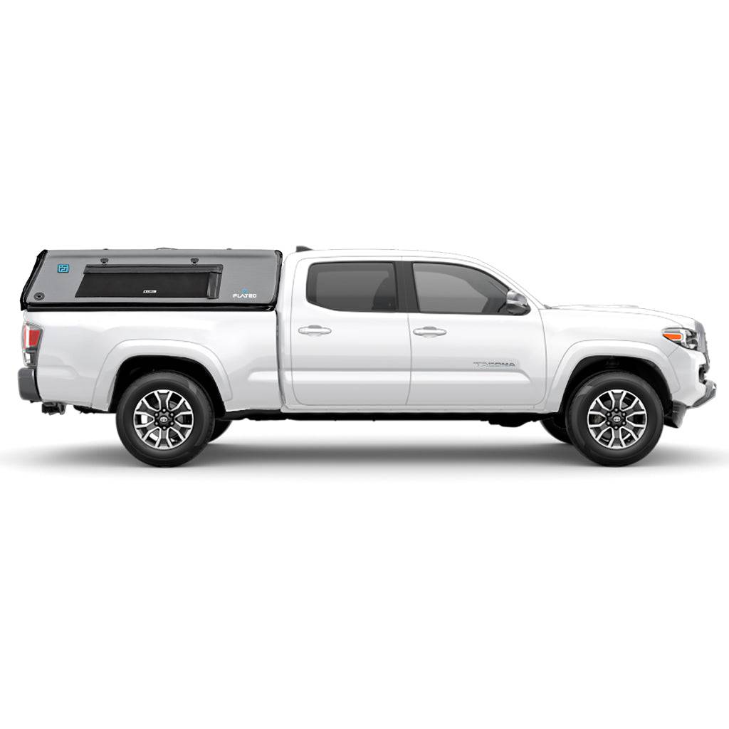 A silver mid-size long bed truck with a gray FLATED MID-LONG CAP60 inflatable camper shell featuring a side window is shown from the side. The truck has black and silver wheels.