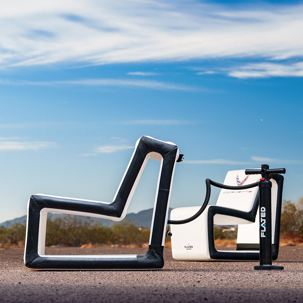 The FLATED COMPACT-SIZE CORVETTE SET includes two modern black and white inflatable chairs plus a hand pump, creating stylish, portable seating for frunk-gating on any paved surface under a clear blue sky.