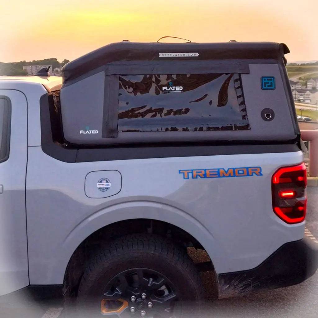 A white pickup truck with TREMOR on the side is fitted with a FLATED COMPACT-MAVERICK MR46 black inflatable truck shell, standing out against a striking sunset backdrop.