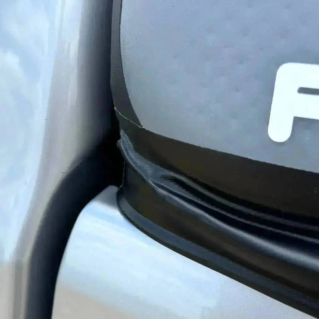 Close-up of a car’s front showing a misaligned panel and black trim, with part of a white letter on gray, possibly near a FLATED MID-SHORT CAP51 inflatable truck cap.