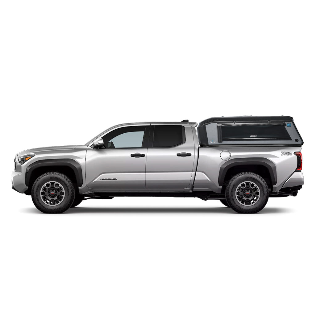 A silver Toyota Tacoma with a 6 ft bed is equipped with FLATED's MID-LONG T24 MR60, a sleek, mid-rise truck topper featuring side windows, off-road tires, and a bold geometric design.