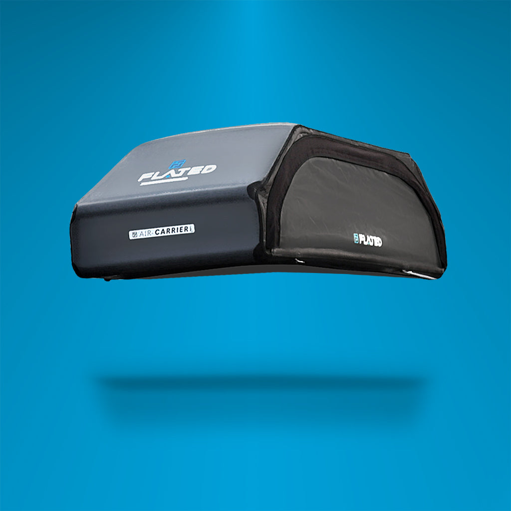 A black, rectangular rooftop cargo carrier with a soft, sleek design is shown floating against a blue gradient background. The carrier has the brand name PLATED on the top and side.