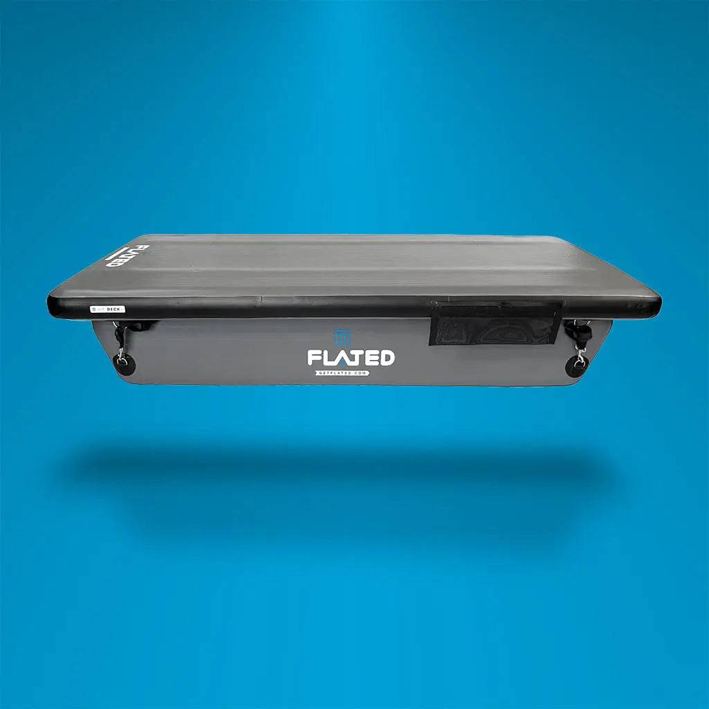 A black FLATED COT DECK60 inflatable sleeping platform with pontoons rests in a white pickup truck bed, set against a backdrop of the adventure rig and trees, showcasing this innovative Air-Deck Cot.