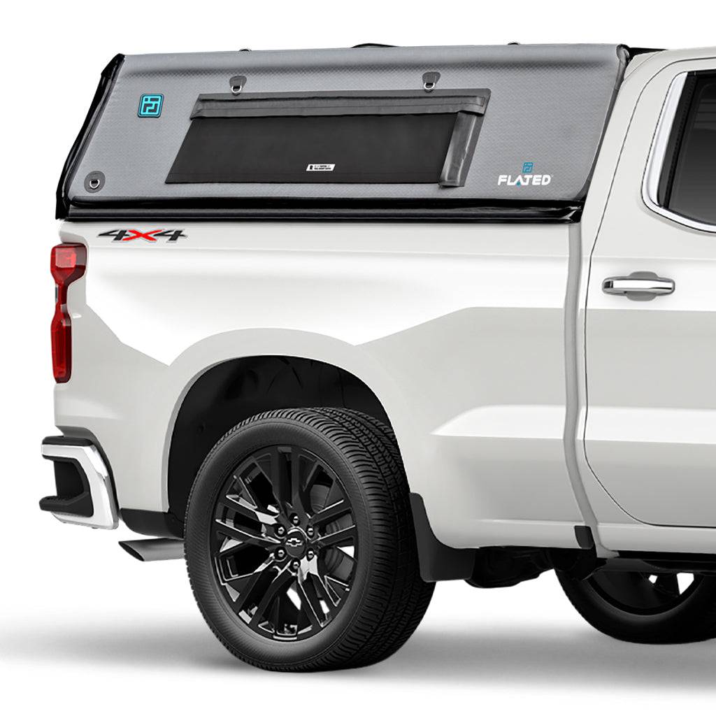 A white pickup truck with a black and gray FLATED FULL-STANDARD CAP66 inflatable truck cap is attached to its full-size bed, shown from a rear side angle. The lightweight shell features a window and prominent FLATED branding labels.