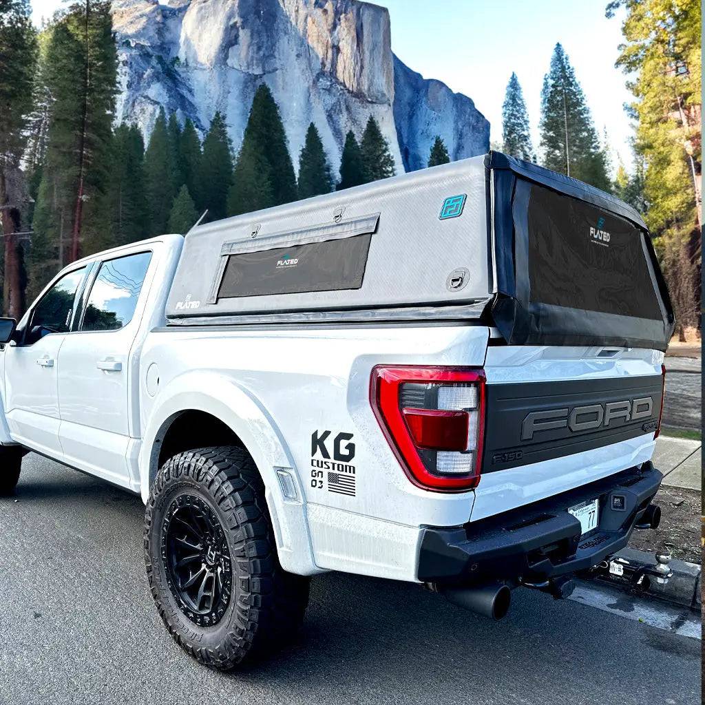 A white pickup truck with a FLATED FULL-SHORT CAP56 (OPEN BOX) black, box-shaped inflatable truck shell on its bed features a side window. The background and truck’s front are softly faded out.
