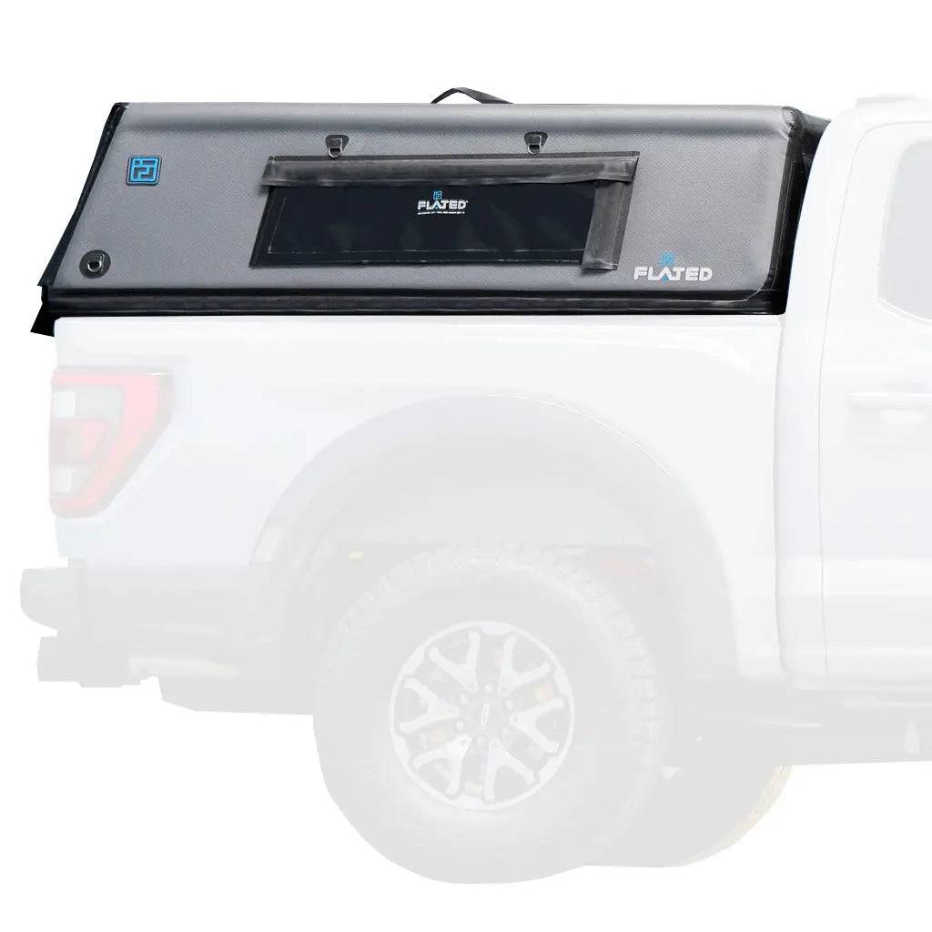 A white pickup truck with a FLATED FULL-SHORT CAP56 (OPEN BOX) black, box-shaped inflatable truck shell on its bed features a side window. The background and truck’s front are softly faded out.