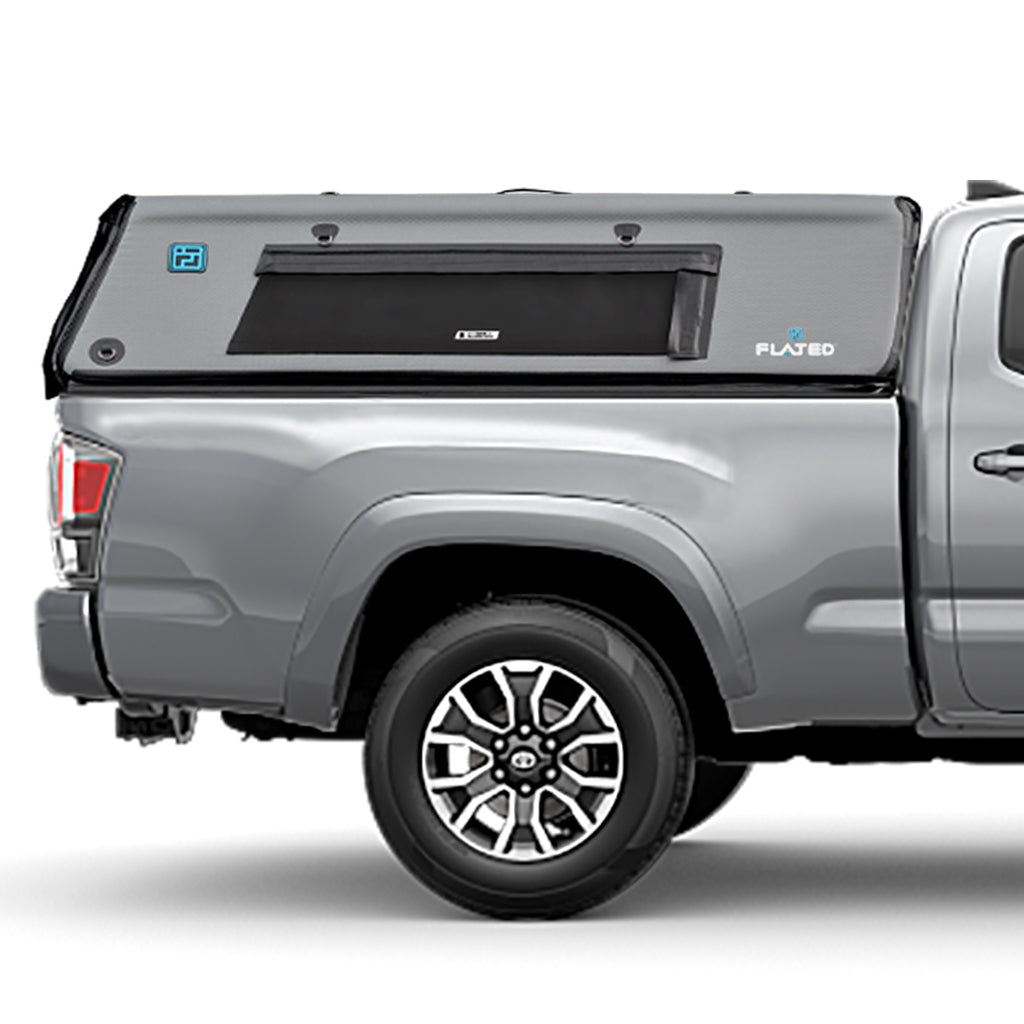 A silver mid-size long bed truck with a gray FLATED MID-LONG CAP60 inflatable camper shell featuring a side window is shown from the side. The truck has black and silver wheels.