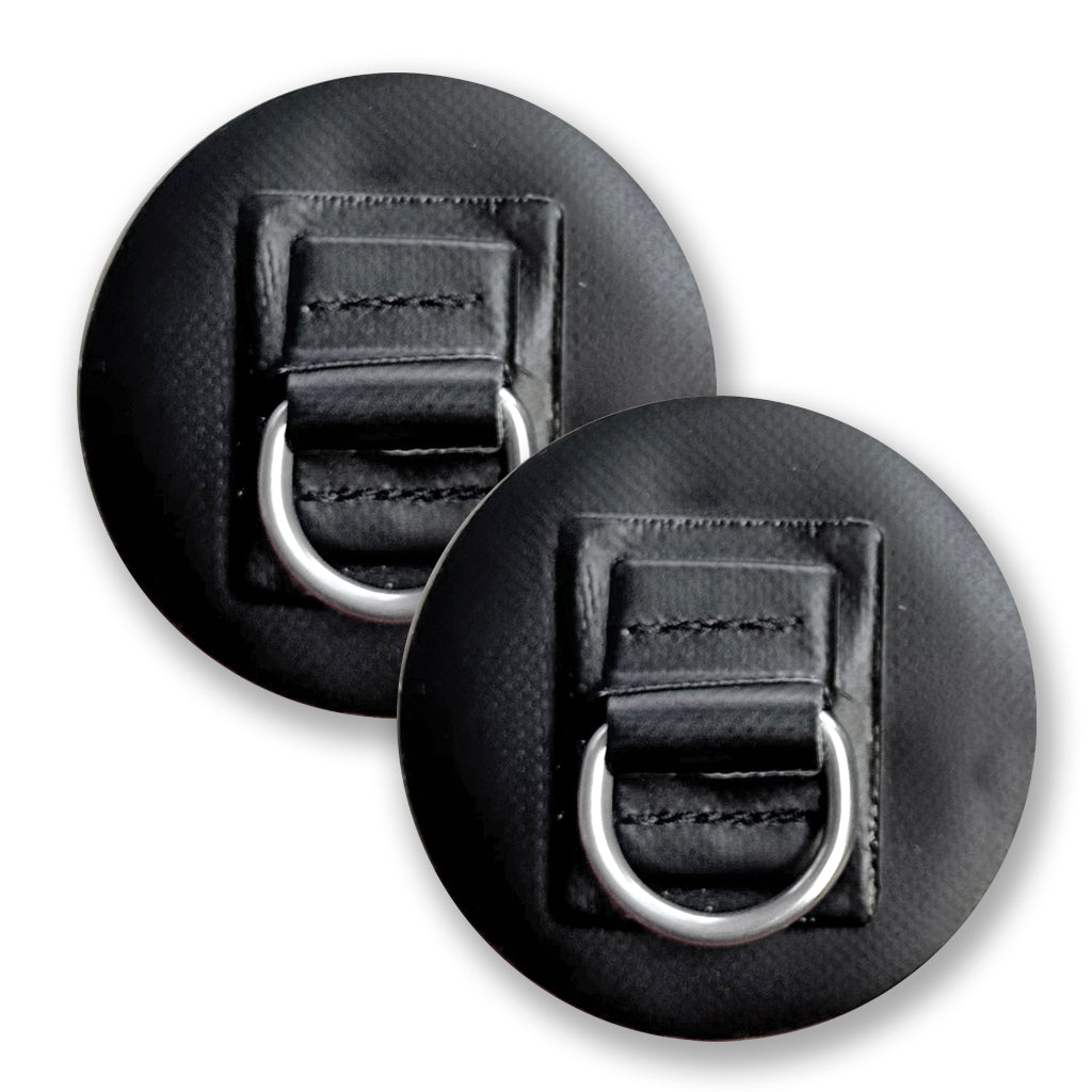 The FLATED D-RING 2PACK includes two black circular patches with stitched rectangular sections, each featuring a silver metal D-ring at the center. These textured, weather-resistant anchor points can be partially overlapped.