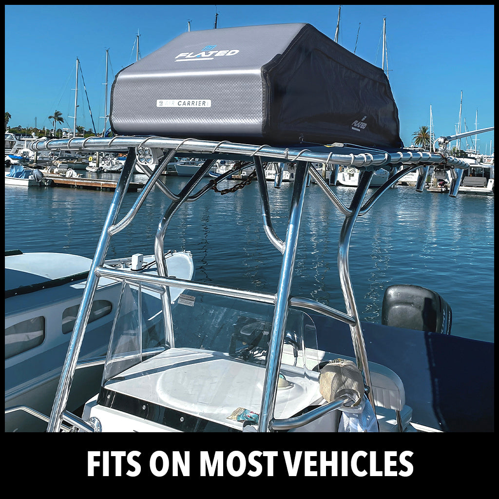 A soft rooftop cargo carrier is mounted on the top frame of a boat docked in a marina, with clear blue water, sailboats, and palm trees in the background. Text at the bottom reads FITS ON MOST VEHICLES.