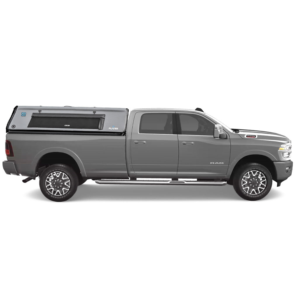 A grey pickup truck with a FLATED FULL-LONG CAP80 black and gray topper attached to the full-size bed, featuring a side window and a 4x4 logo on the rear side. (Mopar Affiliate)