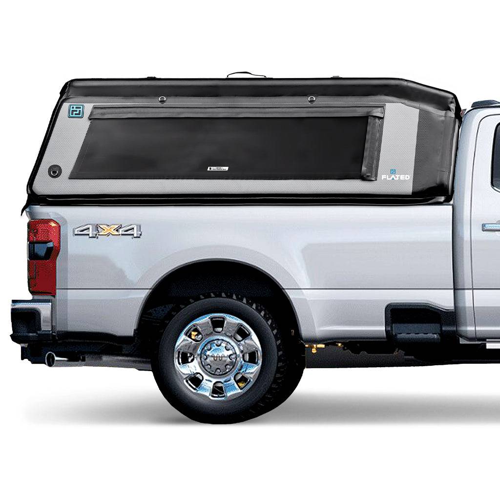 A silver pickup truck with a FLATED FULL-LONG MR80 black and gray topper attached to the full-size bed, featuring a side window and a 4x4 logo on the rear side.