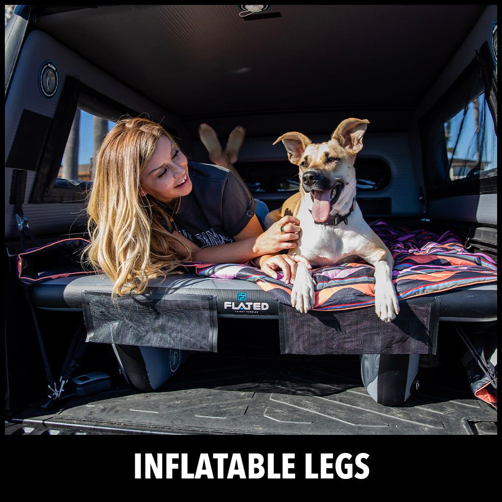 A woman and a happy dog relax on an inflatable mattress inside the back of a vehicle, with sunlight streaming in. The text at the bottom reads INFLATABLE LEGS.