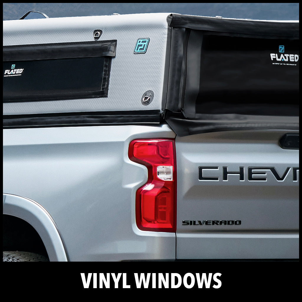 Close-up of a gray Chevy Silverado truck with a Flated camper featuring vinyl windows, parked outdoors. The word VINYL WINDOWS is written at the bottom of the image.
