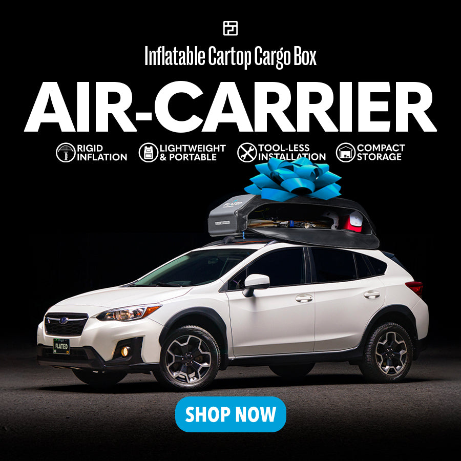 A white SUV with an inflatable rooftop cargo box tied with a blue bow, displaying features like rigid inflation, lightweight, tool-less installation, and compact storage. Text reads AIR-CARRIER and Shop Now.