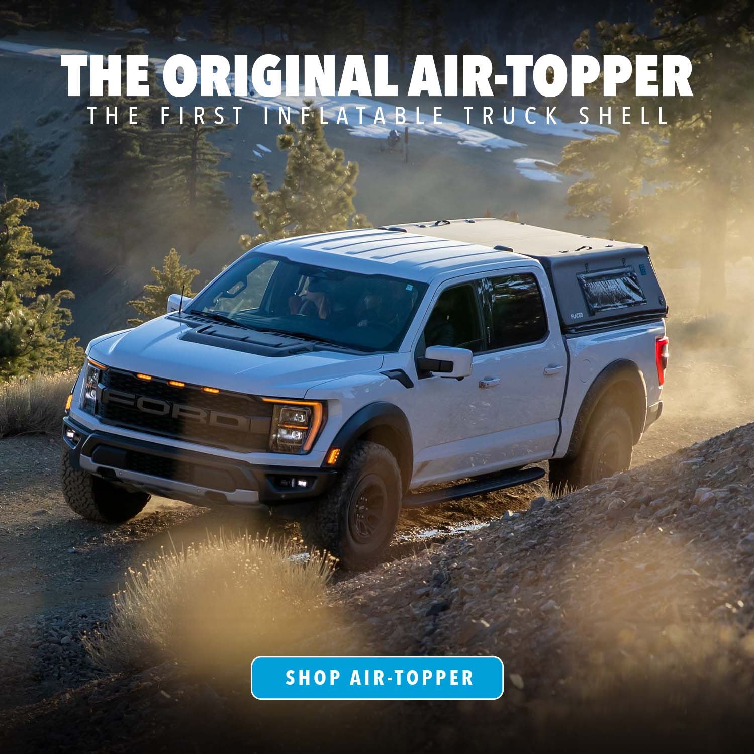 A white Ford pickup truck with an inflatable Air-Topper shell drives on a dusty, rocky off-road trail surrounded by pine trees. Text reads The Original Air-Topper: The first inflatable truck shell.