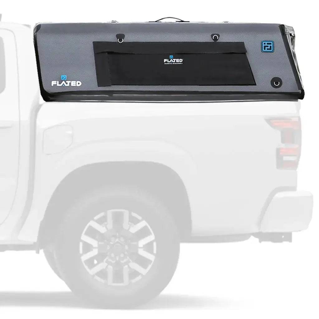 A white pickup truck with a gray, boxy FLATED MID-SHORT CAP411 (OPEN BOX) inflatable truck shell attached to its bed. The topper features a black zippered window and blue logo accents. The background is plain and the truck is in profile.