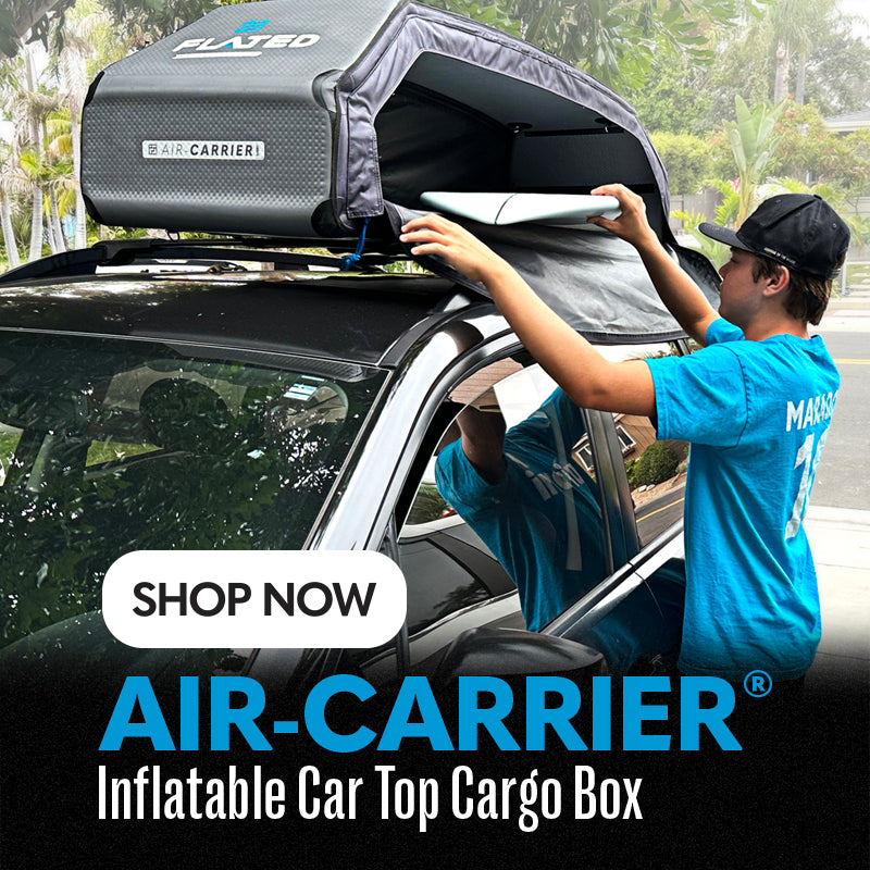 A man wearing a blue shirt opens a gray Air-Carrier inflatable car top cargo box mounted on the roof of a parked car. Trees and greenery are visible in the background. Text reads: “Shop now. Air-Carrier Inflatable Car Top Cargo Box.”.